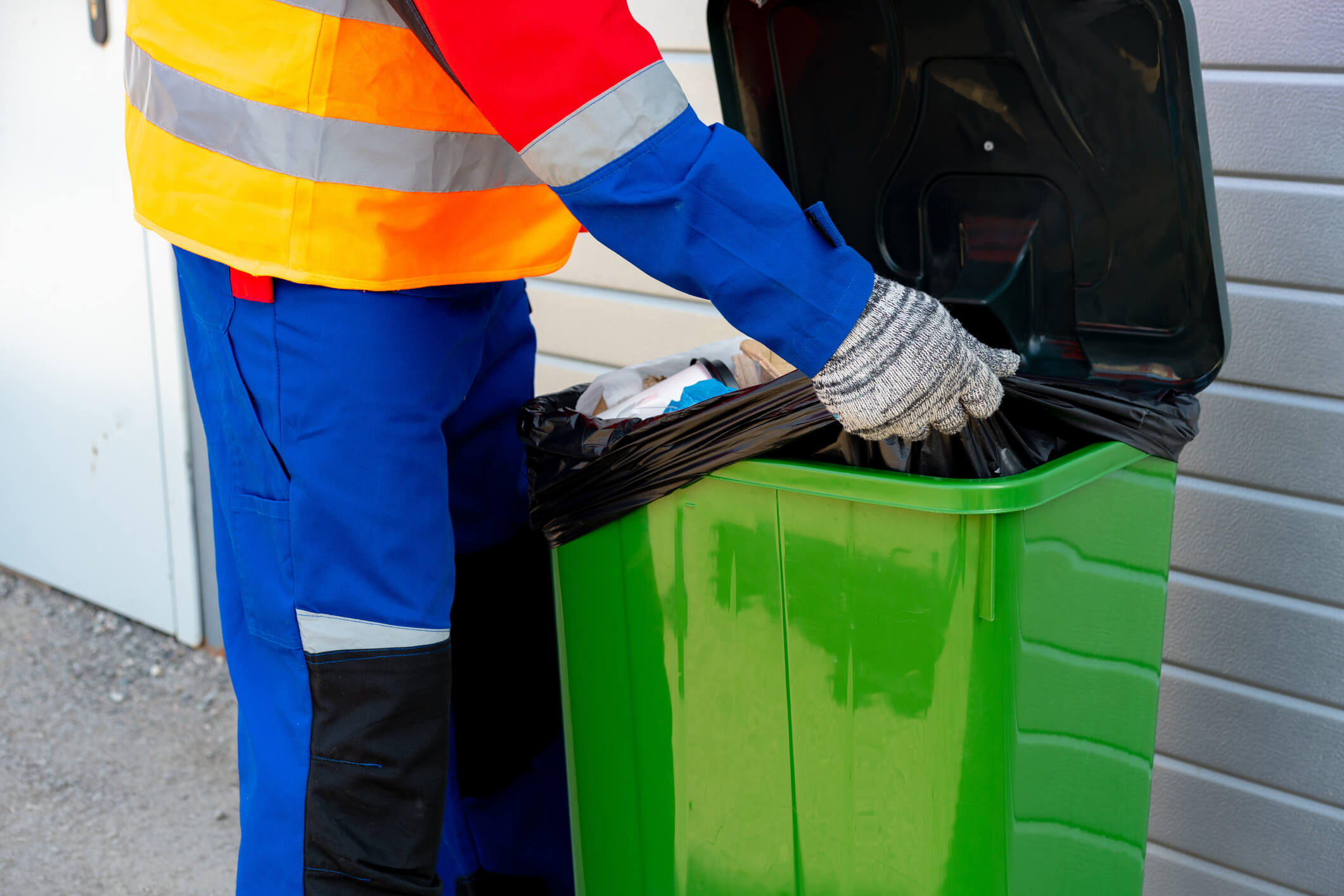 Shows a waste collection operative emptying a wheelie bin